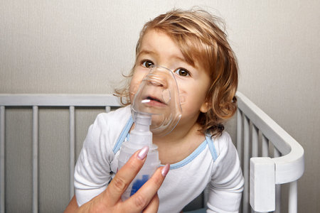 Little white caucasian pretty girl about 1,5 years old is breathing with nebulizer to stop asthma attack. Baby with respiratory diseases are using therapy.の写真素材