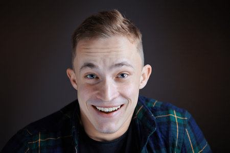 A surprised smile on the face of a young Caucasian man who is see a film in a dark room. The male...