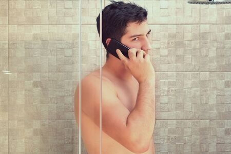 Attractive young caucasian businessman about 22 years old is talking by mobile phone while taking a shower.の写真素材