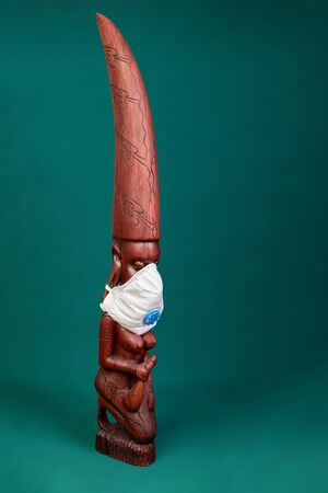A wooden carving of a Masai woman purchased in Tanzania with N95 respirator mask used to protect against covid-19 on it.の写真素材
