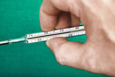 A mans hand holds a mercury thermometer for the body, the scale of which displays a temperature of 39 degrees, which is a high value and indicates a disease.の写真素材