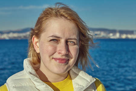 Close-up portrait of a young Caucasian woman with reddish hair and a slight smile on her lips, standing outdoors against backdrop Sea of Marmara and blurry outlines of Istanbul on opposite shore.の写真素材