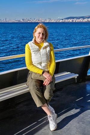 A young Caucasian woman is resting on the deck of a ship that carries passengers to the Princes' Islands of Istanbul by the Sea of Marmara, a sunny winter day.の写真素材