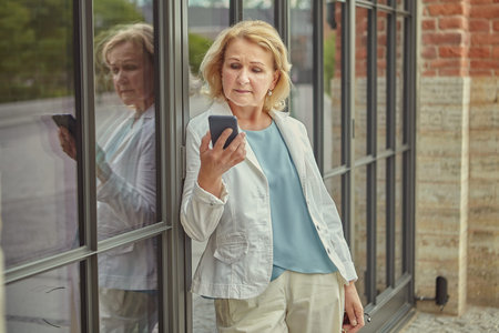 Elderly caucasian pretty business woman about 62 years old with mobile phone in her hand is reading...