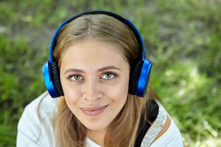 Portrait of beautiful young caucasian cheerful and friendly woman about 25 years old with long blond hair and earphones in public park. Attractive white girl is smiling.の写真素材