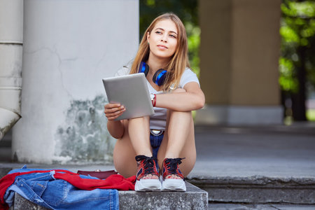 Beautiful young woman is using tablet computer in the public park. Caucasian female about 20 years...
