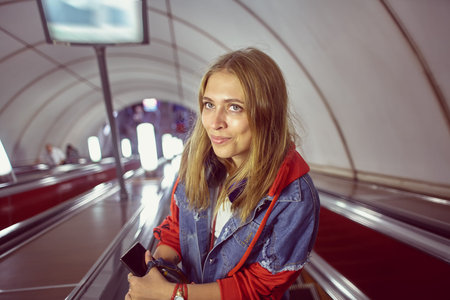 A woman is standing on the escalator that descends to the underground station. Beautiful caucasian...