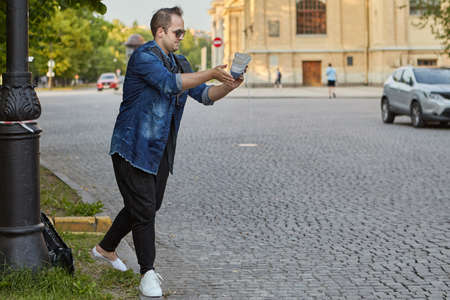 Young man is shaking the sand out of the shoe on the city street. Caucasian male in sunglasses is walking outdoors.の写真素材