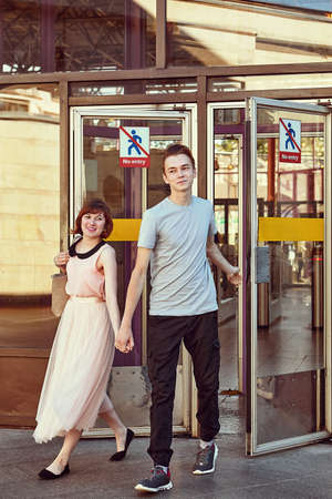 Young caucasian couple is going out underground station hand in hand while man holds a glass door.の写真素材