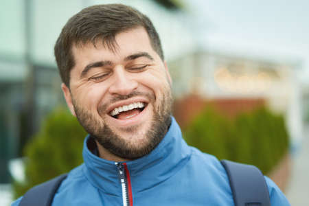 Bearded smiling cheeful young man walks outdoor in blue jacket.の写真素材