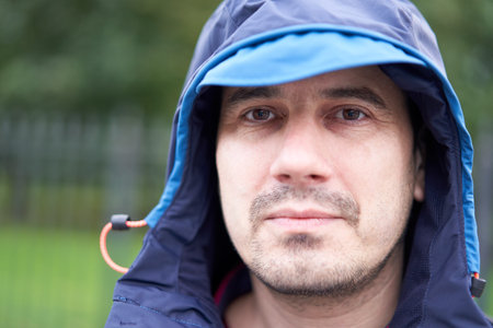 White serious man in blue hood outdoors on blurred background.