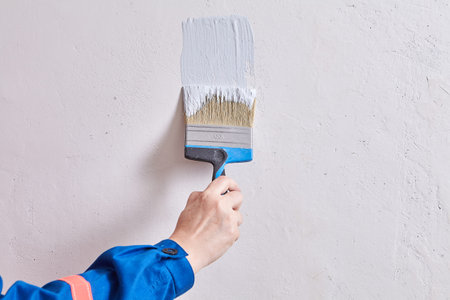 House painter is painting walls with brush and light color during renovation. Handyman paints wall...
