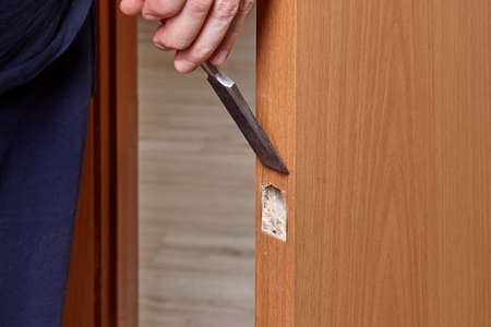 Carpenter cuts slot for door latch plate using chisel.の写真素材