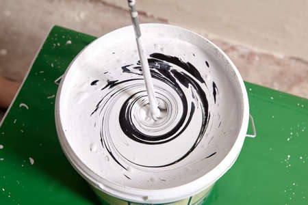 House painter mixes two paints using mixer for bucket with paddle mixing tool.の写真素材