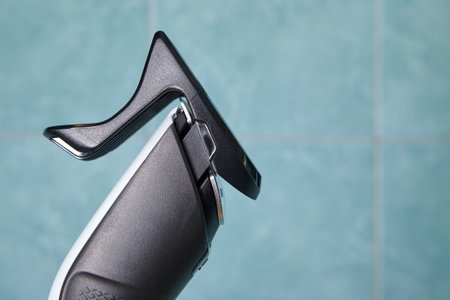 Front part of hair clipper with nozzle on tile background in bathroom.