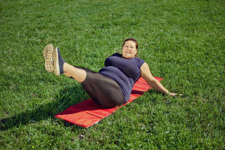 Obese woman does leg raises for weight loss and fit body.の写真素材