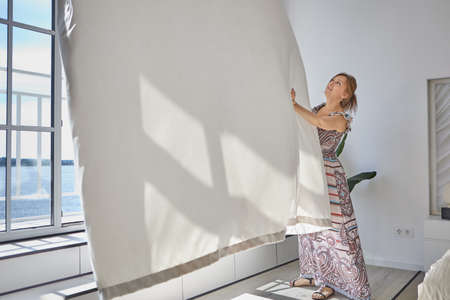 Young lady in casual dress push curtain back.の写真素材