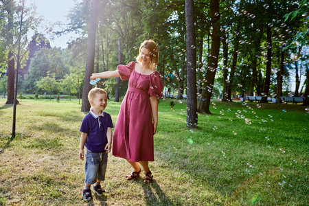 Woman and little son play with bubbles and laugh outdoors.