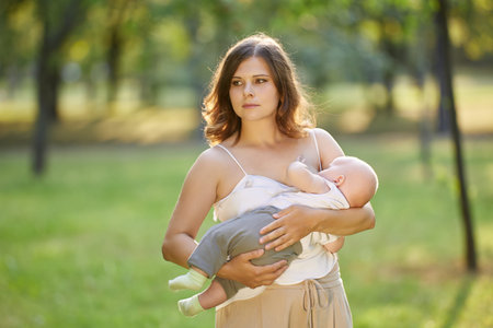 Public breastfeeding by young woman in public park with little child.