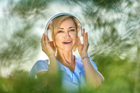 Smiling blond woman in cordless headphones walks in park.