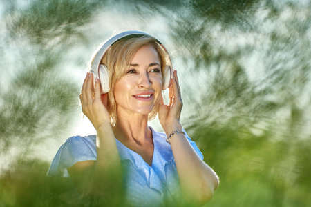 Mature white woman in her 40s listens to music using wireless headphones.の写真素材