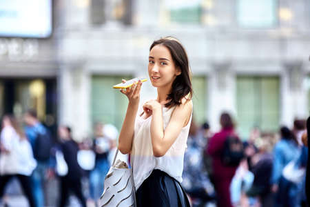 Graceful woman talks by smartphone while walking in city.の写真素材