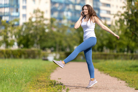 Woman talks by smartphone and makes exercises in park.の写真素材