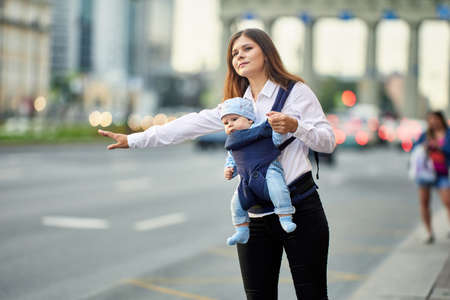 Mother with child in sling is stopping taxi on street.の写真素材