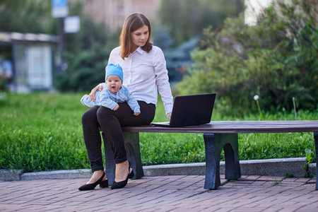 Woman works with laptop with infant on knees outdoors.の写真素材