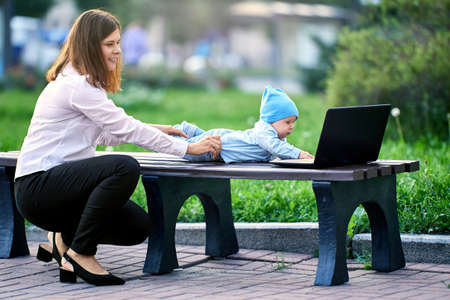 Mother walks with baby and works with laptop in park.の写真素材