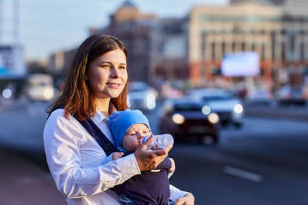 Sling with baby and bottle are hold by woman near traffic.の写真素材