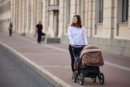 Woman on maternity leave walks with her child in a pram on city street.の写真素材
