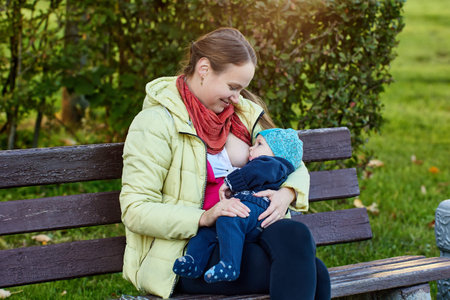 Smiling woman is breastfeeding baby in park.