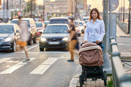 Mother with kid in baby carriage walks near traffic.の写真素材