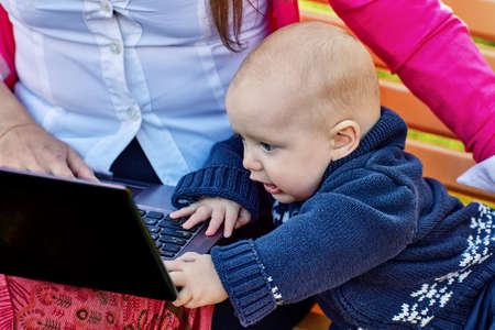 Infant with mother are sitting on bench with laptop.の写真素材