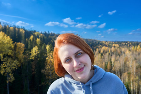 Bob hairstyle on 24 years old red haired woman standing in front of an autumn forest in Russia.
