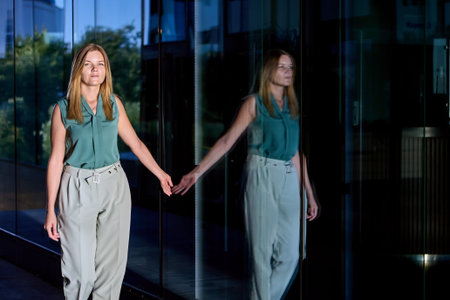Woman is reflected in lass wall of an office building, businesswoman in loose trousers and...