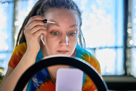 Woman blogger using ring light while online streaming about applying eyebrow lacquer.