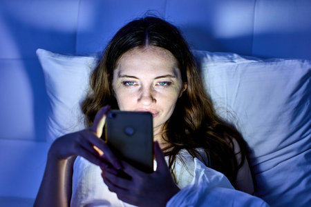 Sad woman with handy is lying in bed and watching video.