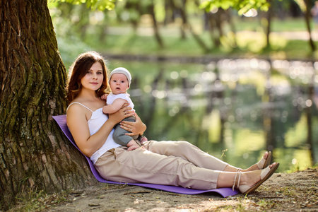 Mother with baby have rest in park at summer day.