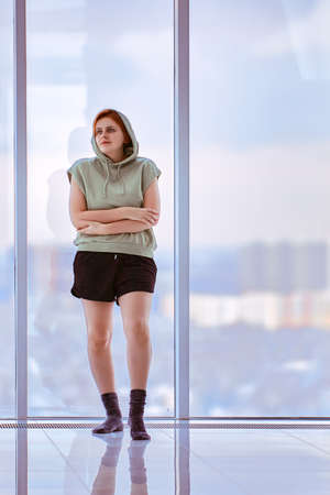 Floor to ceiling windows and woman 26 years old in sportswear stands near.の写真素材