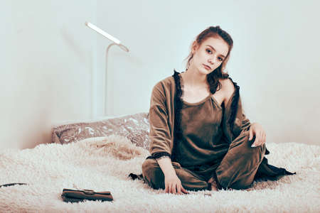 Slender young woman sits on bed in morning dress.の写真素材