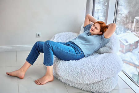 New dwelling for shoeless woman who lies on bean bag chair near floor to ceiling window.の写真素材
