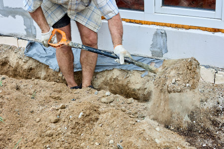 Digging trench for laying cable, construction worker uses shovel to take out soil.
