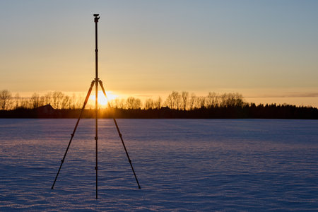Photo equipment, tripod for photo and video filming stands in field in winter at sunset on surface of snow crust.の写真素材