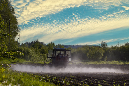 Mist cloud behind an agricultural tractor that applying herbicides into potato field.の写真素材