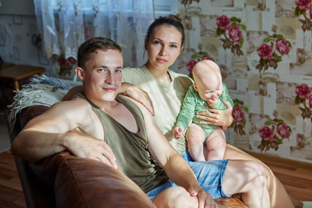 Family portrait of young couple with baby on sofa in living room.