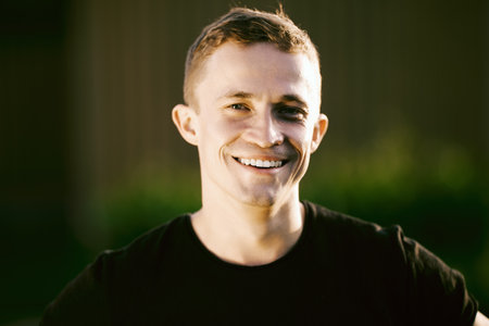 Close up portrait of smiling European man 26 years old outdoors in summer with blurred background.の写真素材