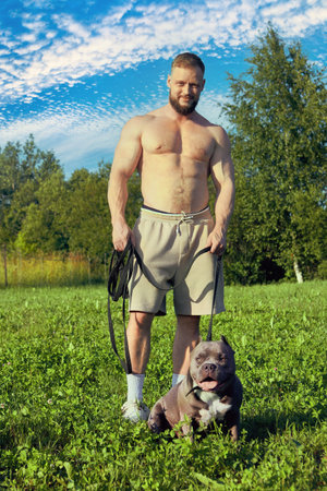 An American Bully walks accompanied by bearded young man in shorts and no shirt.の写真素材