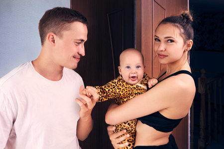 Young parents with six month old baby girl in their home, mother holds her daughter in her arms.